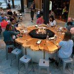 Group gathers around wood table firepit