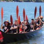 Tribal members in canoe on water with paddles up