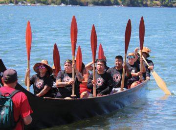Tribal members in canoe on water with paddles up