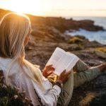Woman reading book on beach at sunset