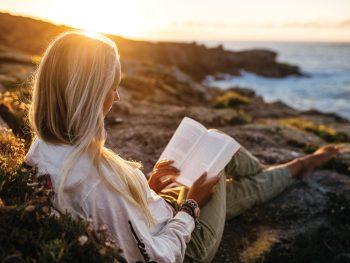 Woman reading book on beach at sunset