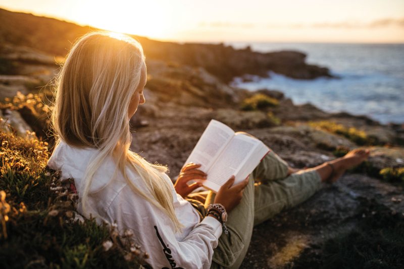 Woman reading book on beach at sunset