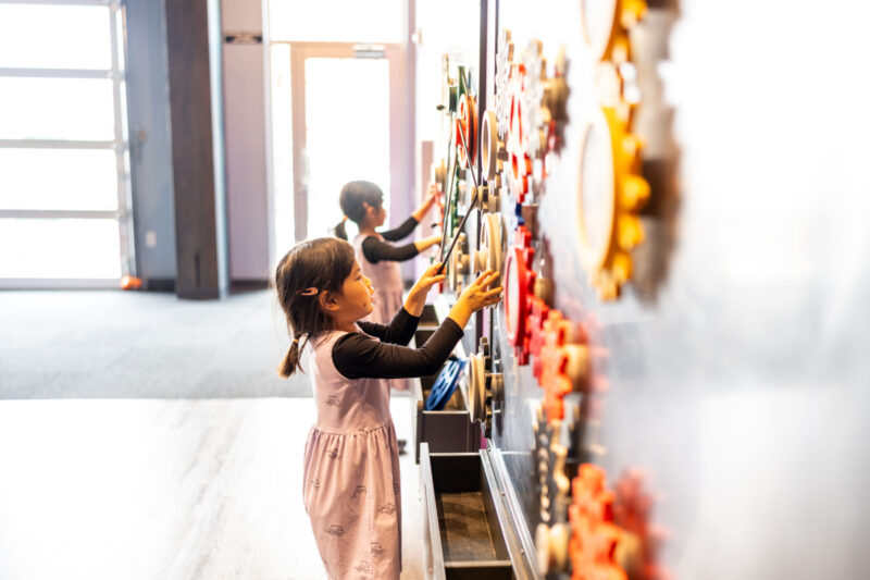 Girl in pink dress experiments with gears at Imagine Childrens Museum