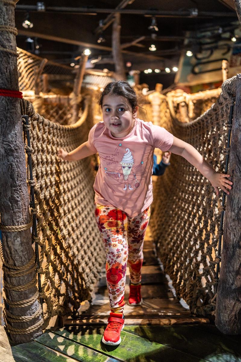 Young girl has fun running across netted bridge at Imagine Childerns Museum